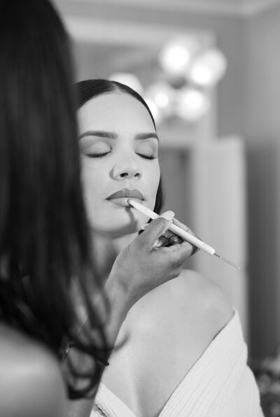 A makeup artist applying lip liner to a woman's face in a black and white photograph.