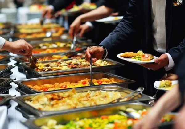 Catering staff serving food from a buffet line to guests at an event.