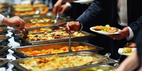 Catering staff serving food from a buffet line to guests at an event.