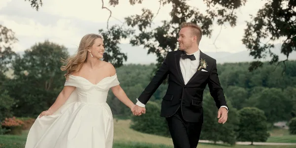 A bride and groom holding hands and walking outdoors in a scenic, natural setting.