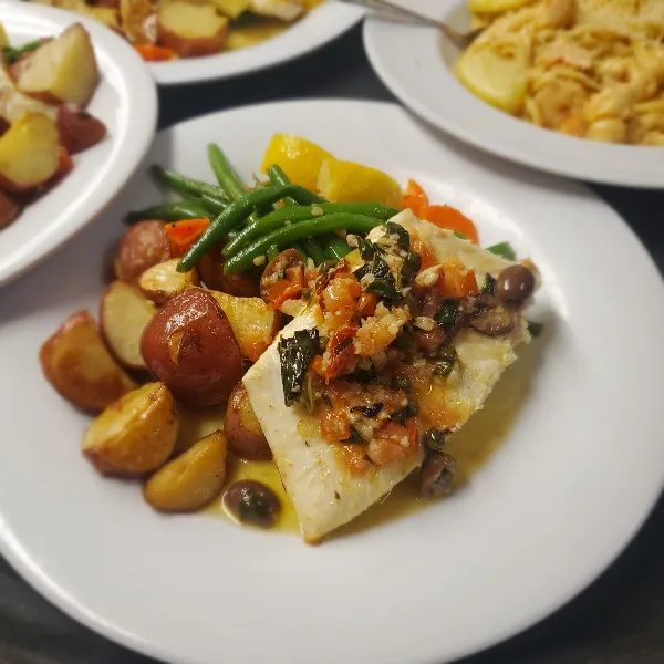 A plate of white fish topped with a tomato and herb relish, served with roasted red potatoes and green beans.