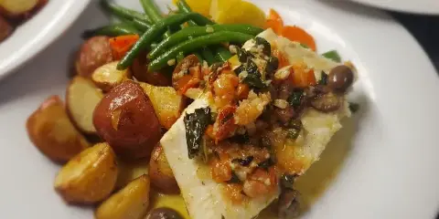 A plate of white fish topped with a tomato and herb relish, served with roasted red potatoes and green beans.