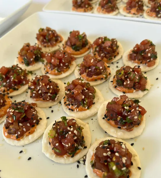 A close-up of a white platter filled with tuna tartare appetizers topped with sesame seeds and herbs.