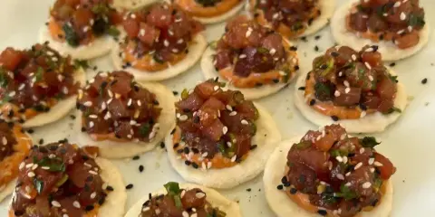 A close-up of a white platter filled with tuna tartare appetizers topped with sesame seeds and herbs.