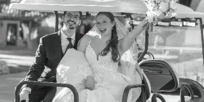 A bride and groom smiling while sitting on a golf cart, with the bride holding a bouquet.