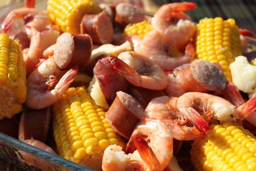 A close-up view of a low country boil containing shrimp, corn on the cob, and sausage.