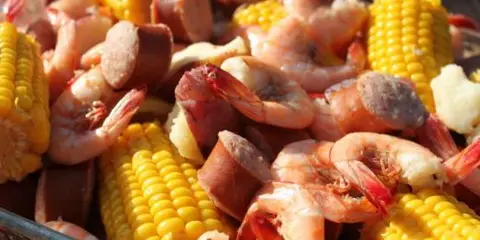 A close-up view of a low country boil containing shrimp, corn on the cob, and sausage.