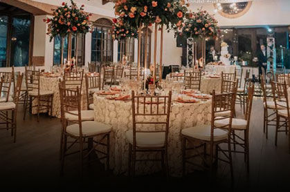 An indoor event space set up with round tables, white linens, Chiavari chairs, and tall floral centerpieces.