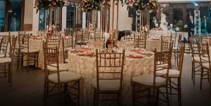 An indoor event space set up with round tables, white linens, Chiavari chairs, and tall floral centerpieces.