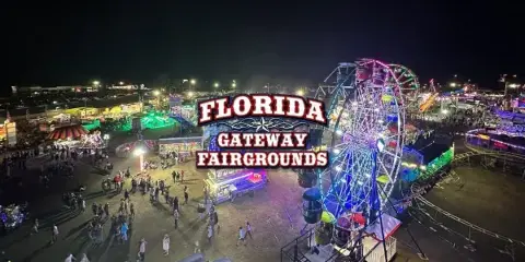 Aerial night view of the Florida Gateway Fairgrounds featuring a lit Ferris wheel, carnival rides, and crowds of people.