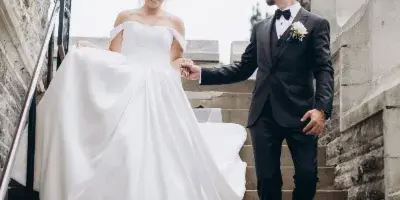 A bride in a white gown and a groom in a black tuxedo walking down stone steps while holding hands.