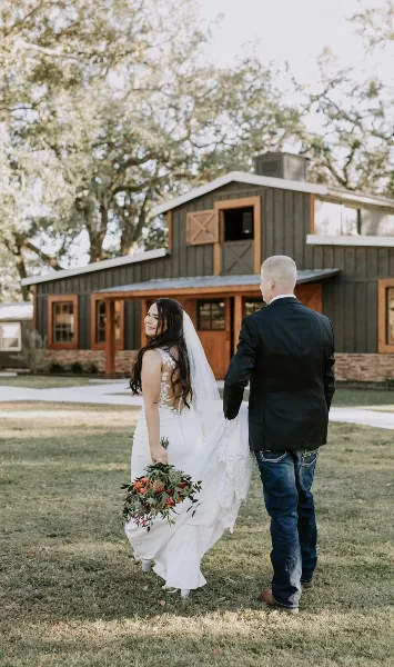 A bride and groom standing on a lawn in front of a rustic wooden barn venue.