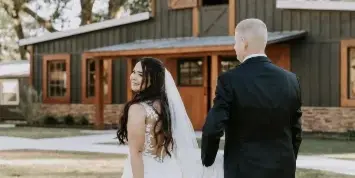 A bride and groom standing on a lawn in front of a rustic wooden barn venue.