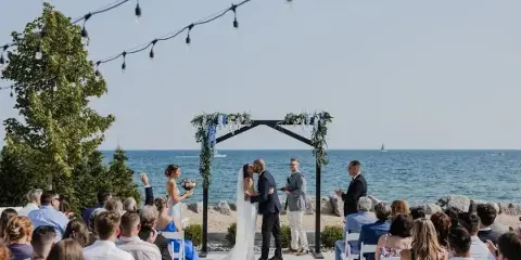 A wedding ceremony in progress on a beachfront patio with a view of the lake and a decorated arch.