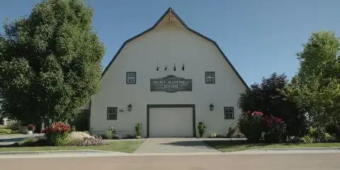 Exterior view of the white gambrel-roofed Mint Barrel Barn with a sign on the facade.