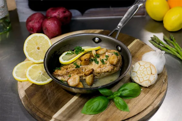 A plated dish of salmon with lemon and garlic, garnished with herbs, on a wooden board.