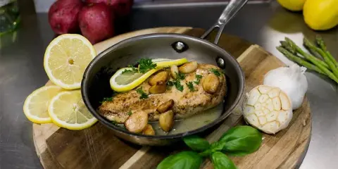 A plated dish of salmon with lemon and garlic, garnished with herbs, on a wooden board.