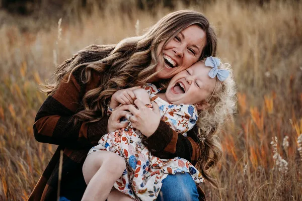 A smiling woman holding a laughing young child in a field of tall dry grass.