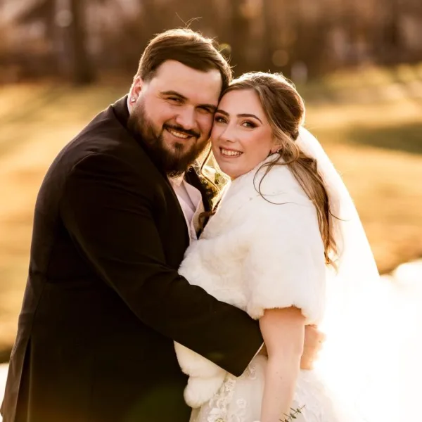 A professional wedding photograph of a smiling bride and groom embracing outdoors.