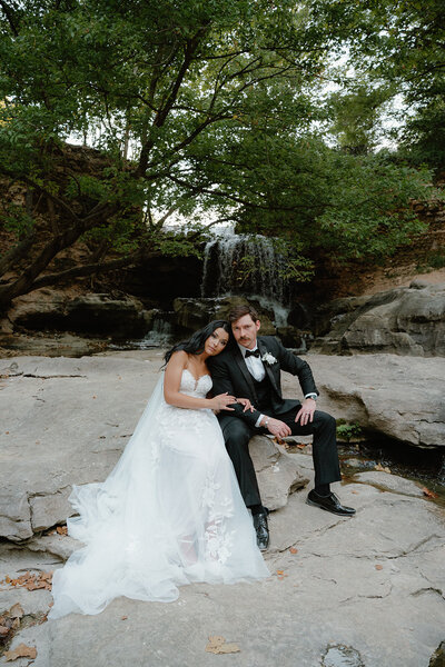 Bride and groom sitting on a rock in front of a waterfall