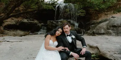 Bride and groom sitting on a rock in front of a waterfall