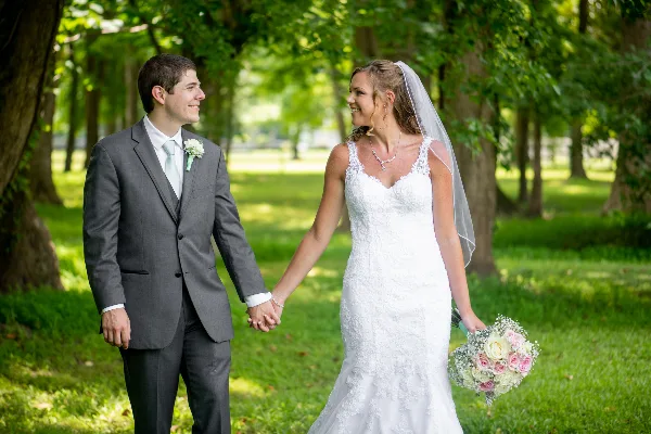 A bride and groom holding hands and smiling at each other in a park setting.
