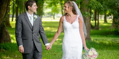 A bride and groom holding hands and smiling at each other in a park setting.