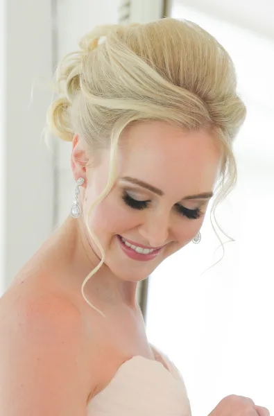 A smiling blonde bride with an elegant updo hairstyle and professional makeup.