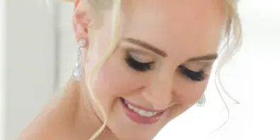 A smiling blonde bride with an elegant updo hairstyle and professional makeup.