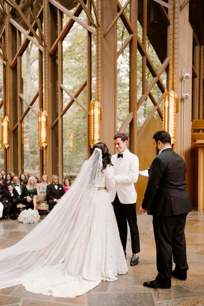 A bride and groom exchanging vows during a wedding ceremony in a chapel with guests seated in the background.