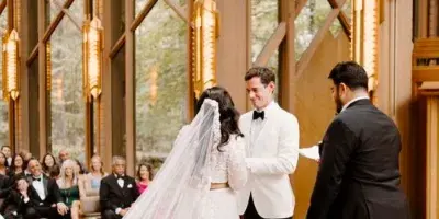 A bride and groom exchanging vows during a wedding ceremony in a chapel with guests seated in the background.