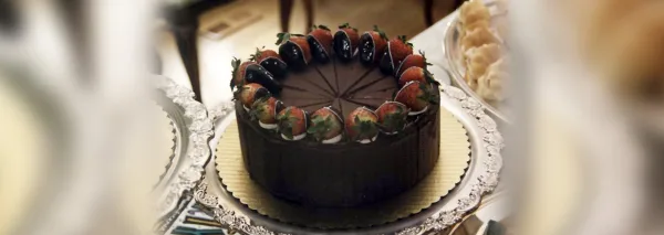 A round chocolate cake topped with a ring of strawberries and cream, served on a silver platter.
