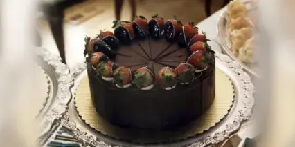 A round chocolate cake topped with a ring of strawberries and cream, served on a silver platter.