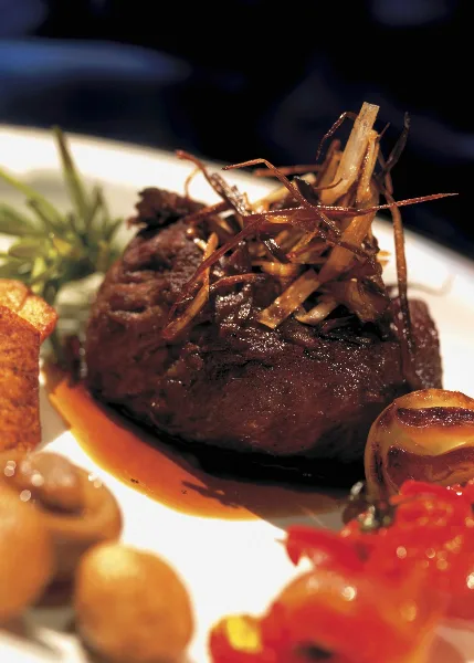 A plated gourmet dish featuring a meat medallion topped with caramelized onions, served with roasted vegetables and a rich sauce.