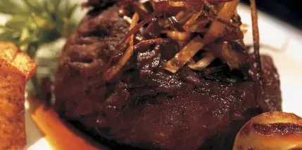 A plated gourmet dish featuring a meat medallion topped with caramelized onions, served with roasted vegetables and a rich sauce.
