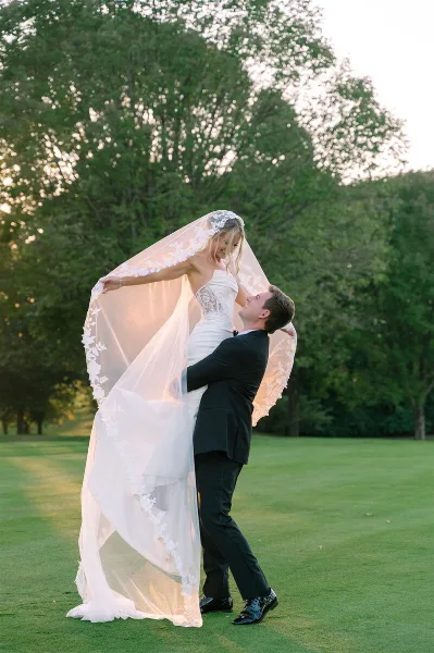 A bride and groom dancing on a green lawn with the bride's veil flowing in the air.