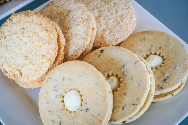 A close-up photograph of a white plate holding several round, baked cookies, some with a white cream filling in the center.