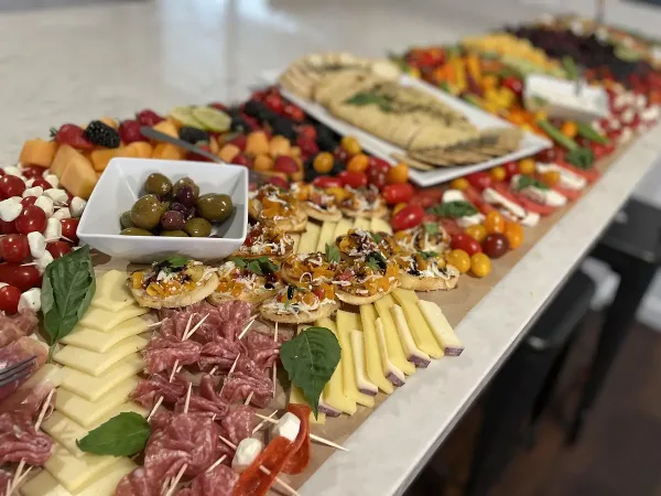 A long, styled grazing table featuring an assortment of cheeses, cured meats, fresh fruit, and crackers arranged for an event.