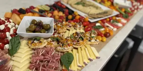 A long, styled grazing table featuring an assortment of cheeses, cured meats, fresh fruit, and crackers arranged for an event.
