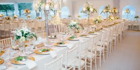 Interior of a white event tent featuring long banquet tables with white linens and rows of white Chiavari chairs.