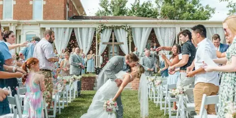 A bride and groom share a kiss at the end of their wedding aisle while guests throw flower petals.