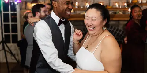 A bride and groom laughing and dancing together at a wedding reception.