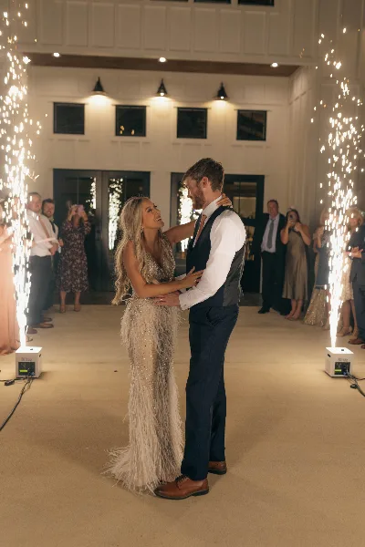 A bride and groom dancing at a wedding reception surrounded by cold sparklers and guests.