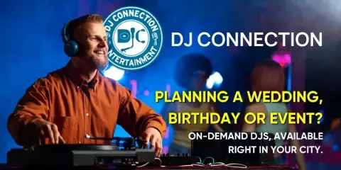 A DJ wearing headphones and an orange shirt operating a turntable at an event with a dance floor and blue lighting in the background.
