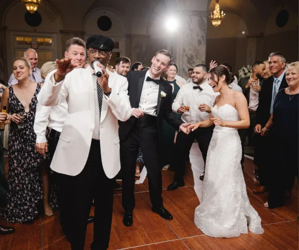 A live wedding band performing at a reception, with the lead singer interacting with the bride and groom on the dance floor.
