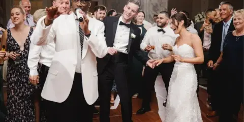 A live wedding band performing at a reception, with the lead singer interacting with the bride and groom on the dance floor.