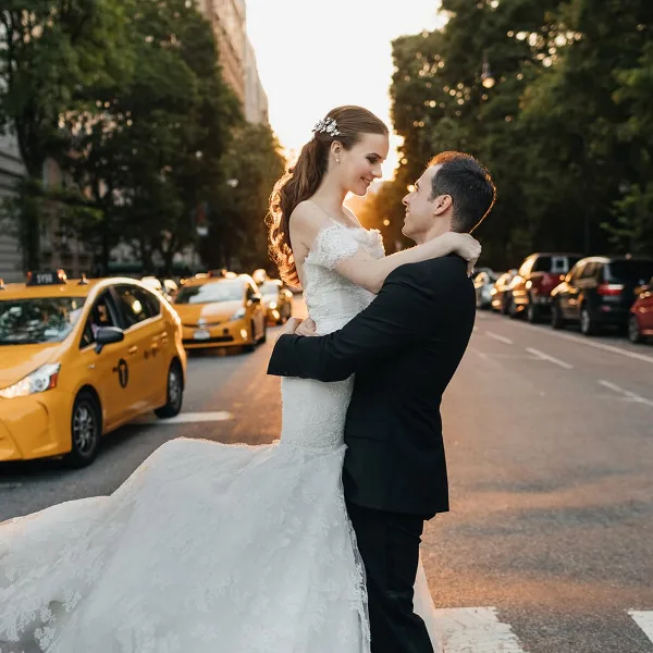 A bride and groom embracing on a city street with yellow taxis in the background.