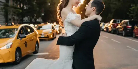 A bride and groom embracing on a city street with yellow taxis in the background.