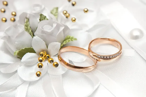 Rose gold wedding rings and a white floral boutonniere resting on white fabric.