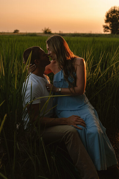 A couple sharing a kiss in a field at sunset, photographed by a professional photographer.